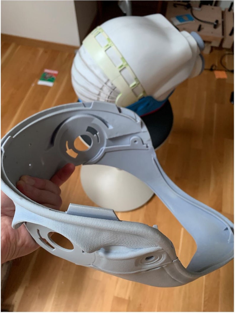 May include: A light gray plastic helmet with a textured surface and several holes. The helmet is designed to fit around the head and neck.