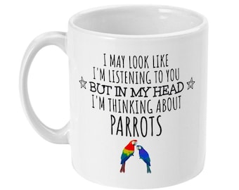 May include: White ceramic mug with a black and white text design that reads "I may look like I'm listening to you but in my head I'm thinking about parrots". The mug features a colorful parrot illustration.