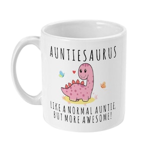 May include: White ceramic mug featuring a pink dinosaur illustration and the text "Auntieosaurus Like a normal auntie, but more awesome!"