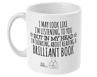 May include: White ceramic mug with black text that reads "I may look like I'm listening to you but in my head I'm thinking about reading a brilliant book". A simple line drawing of a person reading a book is below the text.