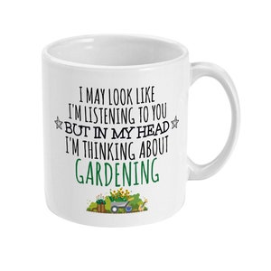 May include: White ceramic mug with a curved handle. The mug features the text "I MAY LOOK LIKE I'M LISTENING TO YOU BUT IN MY HEAD I'M THINKING ABOUT GARDENING" in black and green. A small garden scene is at the bottom.