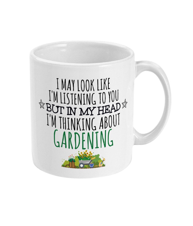 May include: White ceramic mug with a curved handle. The mug features the text "I MAY LOOK LIKE I'M LISTENING TO YOU BUT IN MY HEAD I'M THINKING ABOUT GARDENING" in black and green. A small garden scene is at the bottom.