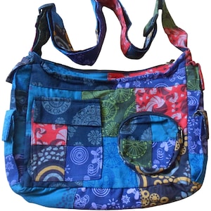 May include: A patchwork shoulder bag in shades of blue, red, green, and purple. The bag features a variety of patterned squares, two front pockets, and a small round zippered pouch. The adjustable strap is multi-coloured.