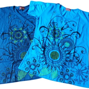 May include: Two blue t-shirts with a floral design in black and green. The design features large, intricate flowers with a central circle and radiating petals.