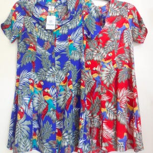 May include: Two short-sleeved dresses with a tropical parrot and leaf print. One dress is blue, the other is red. Both have a V-neck and are hanging on a black hanger. The dresses have a button-up front.