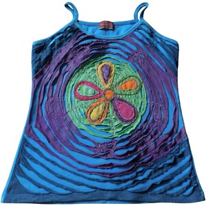 May include: A blue tank top with a colourful flower design in the centre. The flower is made of different coloured fabric pieces sewn together. The top has a distressed look with ripped edges.