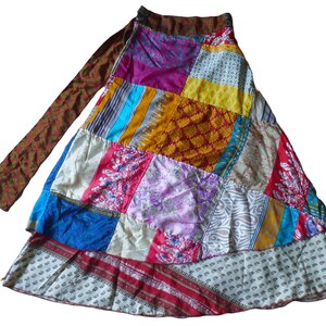 May include: A patchwork skirt with a wrap-around design. The skirt features a variety of colourful fabric patches in shades of pink, blue, yellow, and red. The skirt has a long, patterned tie and a layered hemline.