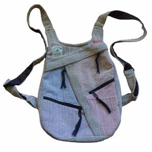 May include: A grey and pink hemp backpack with black straps and zipped pockets. The backpack has a small green leaf logo with the text "Himalayan Hemp" on it.