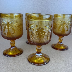 May include: Set of four amber glass goblets with a floral design. The goblets have a textured surface and a stemmed base.