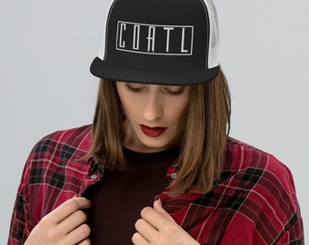 May include: Black and white trucker hat with the word "COATL" in a white rectangular box. The hat has a black brim and a white mesh back. The person in the image is wearing a red and black plaid shirt.