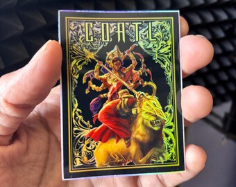 May include: A rectangular sticker with a black background and a gold border. The sticker features a colorful illustration of a deity riding a lion, with the word "COATL" at the top. The sticker has a holographic effect.