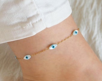May include: Gold chain anklet with blue evil eye charms. The anklet is on a person's ankle.