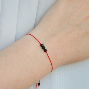 Puede incluir: Un brazalete de cuerda roja con tres cuentas negras facetadas.