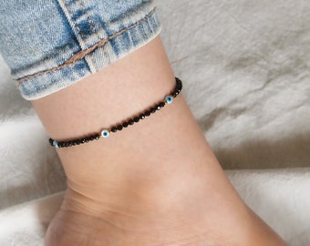 May include: Black anklet with small black beads and blue evil eye charms.