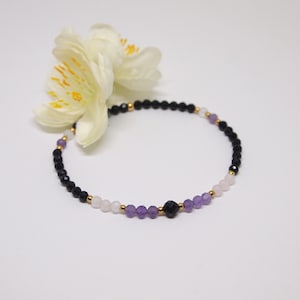 May include: A delicate bracelet with black onyx, amethyst, and rose quartz beads. The bracelet is accented with gold spacers.