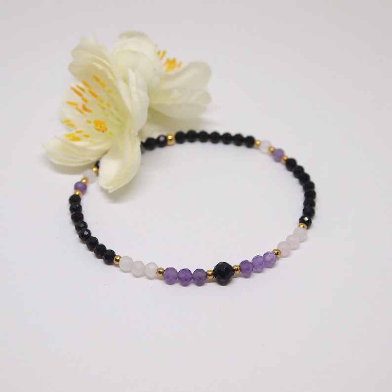 May include: A delicate bracelet with black onyx, amethyst, and rose quartz beads. The bracelet is accented with gold spacers.