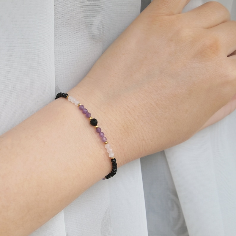 May include: A bracelet with black, white, and purple beads. The beads are strung on a black cord.