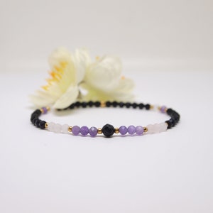 May include: A beaded bracelet with black, purple, and pink beads separated by gold spacers.