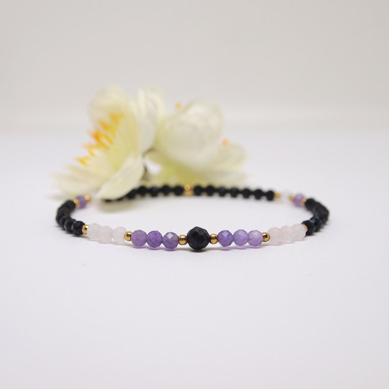 May include: A beaded bracelet with black, purple, and pink beads separated by gold spacers.