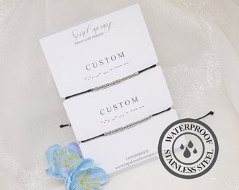 May include: Two black string bracelets with silver beads spelling out "CUSTOM" in Morse code. The bracelets are displayed on a white card with the text "Secret message morse code bracelet". A black and white sticker with the text "WATERPROOF STAINLESS STEEL" and three water drops is in the lower right corner.