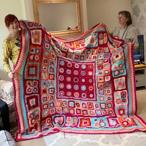 May include: A large, colorful crocheted blanket with a geometric pattern in shades of pink, orange, blue, and white.