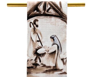 May include: A white kitchen towel with a brown and white illustration of the nativity scene. The illustration depicts Mary, Joseph, and the baby Jesus in a stable.