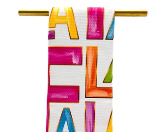 May include: A white kitchen towel with a colorful alphabet pattern. The letters are outlined in gold and are in various shades of pink, blue, yellow, green, and orange.