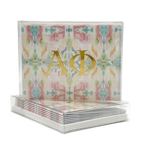 May include: A stack of boxed note cards with a pink, green, and white patterned design. The top card features the letters "AΦ" in gold foil.