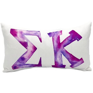 May include: White pillow with a watercolor design of the Greek letters Sigma Kappa in shades of purple and pink.