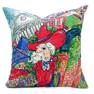 May include: A colorful throw pillow featuring a cartoon illustration of a man wearing a red hat and suit, standing in front of a building with a clock tower. The background includes a cityscape with red, blue, and green accents.
