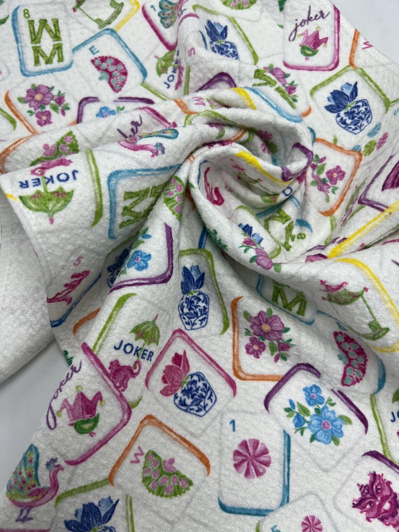 K&ouml;nnte beinhalten: Wei&szlig;er Stoff mit einem farbenfrohen Muster aus Mahjong-Steinen, Blumen und dem Wort "Joker". Die Kacheln sind in verschiedenen Farben umrandet, mit floralen und geometrischen Designs. Der Stoff ist gefaltet und zeigt das sich wiederholende Muster.