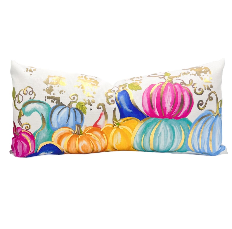 May include: A white lumbar pillow with a colourful autumnal design featuring gourds and pumpkins in shades of pink, blue, orange, yellow, and green. The design is accented with gold leaf.
