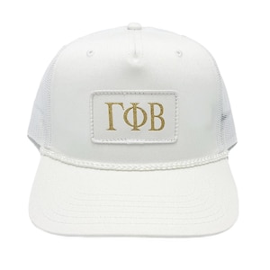 Könnte beinhalten: Weißer Trucker-Hut mit Mesh-Rückseite und gebogenem Schirm. Der Hut hat einen rechteckigen Aufnäher mit den goldenen Buchstaben "ГФВ". Der Hut hat ein weißes Seildetail entlang des Schirms.
