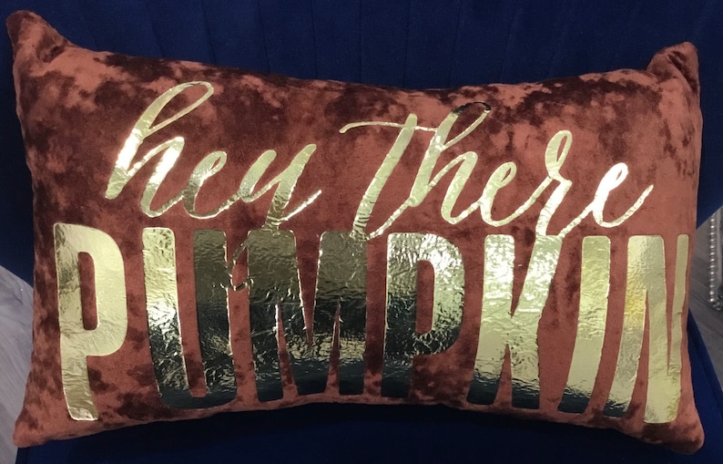 May include: A brown velvet pillow with the words "hey there pumpkin" in gold foil lettering.