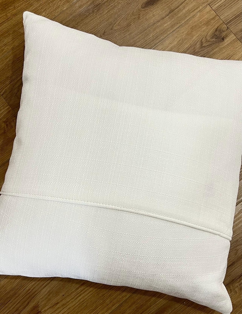 May include: A square throw pillow cover in a solid off-white color. The fabric features a visible woven texture and a horizontal seam running across the middle, indicating a hidden flap closure design on the back side of the pillow cover.