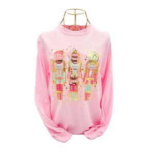 May include: Pink long-sleeved t-shirt with a gold foil print of three nutcracker figures.