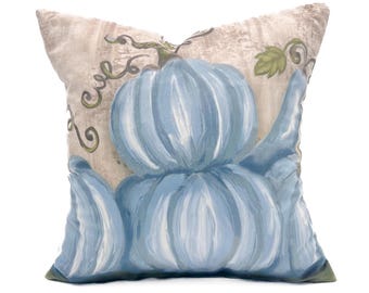 May include: A decorative throw pillow with a blue and white pumpkin design. The pillow has a beige background with a subtle texture.