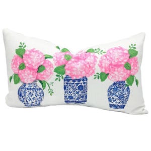May include: White rectangular pillow featuring a floral design. The pillow displays three blue and white vases filled with pink hydrangea flowers and green leaves. The vases have intricate patterns.