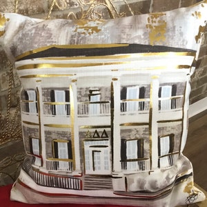 Pu&ograve; includere: Un cuscino bianco con un'illustrazione dorata di una casa con una porta bianca e finestre nere. La casa ha un'iscrizione dorata che dice "AAA".