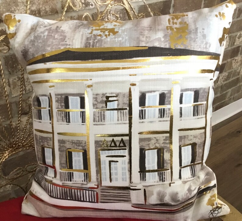 Pu&ograve; includere: Un cuscino bianco con un'illustrazione dorata di una casa con una porta bianca e finestre nere. La casa ha un'iscrizione dorata che dice "AAA".