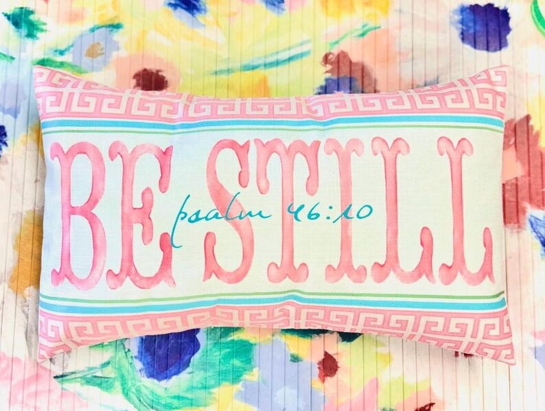 May include: A light green and pink pillow with a white border and a pink "BE STILL" inscription with the text "psalm 46:10" in blue underneath.