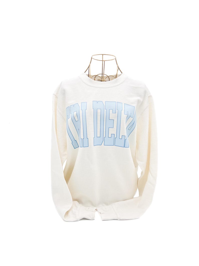 Op de afbeelding: Witte longsleeve waffle-trui met een blauwe "CHI DELTA" print.