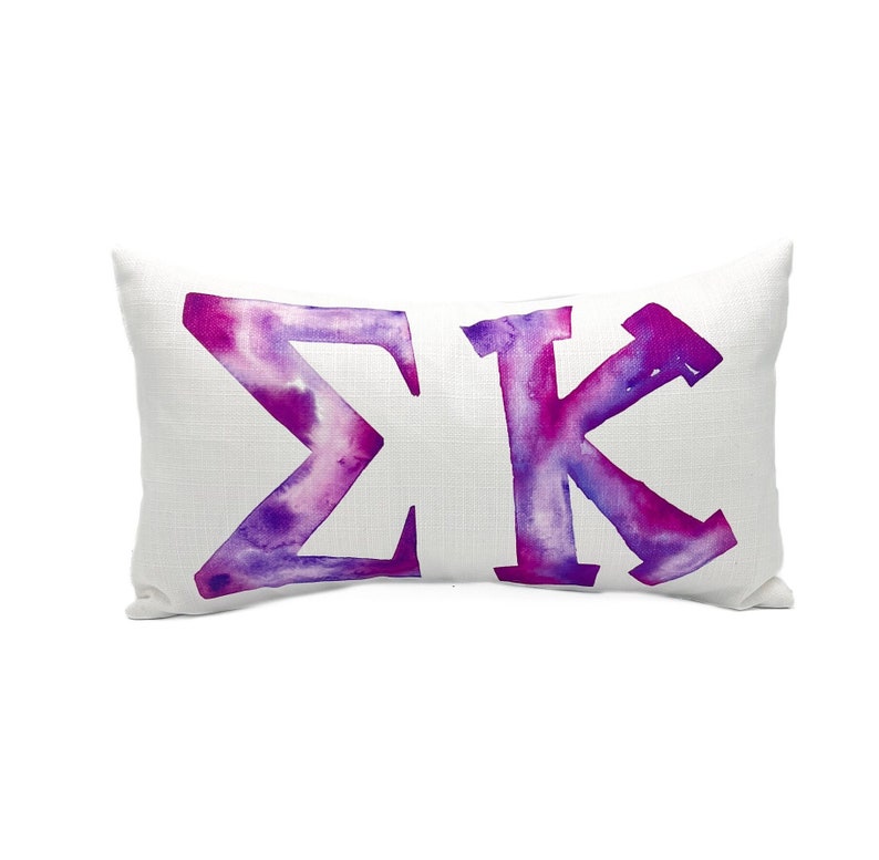 May include: White pillow with a watercolor design of the Greek letters Sigma Kappa in shades of purple and pink.