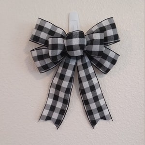 May include: A black and white checkered bow with a white center. The bow is attached to a white hook.