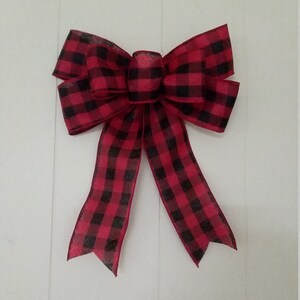 May include: A large red and black plaid bow with a center loop. The bow is made of a soft, textured fabric.