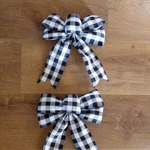 May include: Two black and white checkered bows with long tails. The bows are made of ribbon and are tied in a classic bow shape.