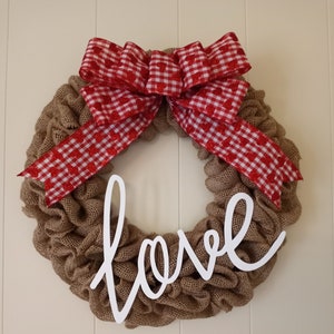 May include: A burlap wreath with a red and white gingham bow and the word "love" in white script.