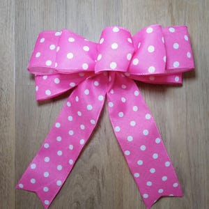 May include: A bright pink bow with white polka dots. The bow is made of a satin-like material and has long, pointed tails. The bow is a decorative item, suitable for gift wrapping or crafting.