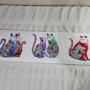 Könnte beinhalten: Ein weißes rechteckiges Kissen mit drei Paaren bunter Katzen mit Paisley-Mustern. Die Katzen sind in Blau-, Rot-, Lila- und Grüntönen gehalten. Die Ränder haben ein schwarz-weißes Paisley-Design.