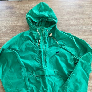 May include: A green hooded jacket with a zipper closure and a small anchor logo on the front. The jacket has a drawstring hood and elastic cuffs.